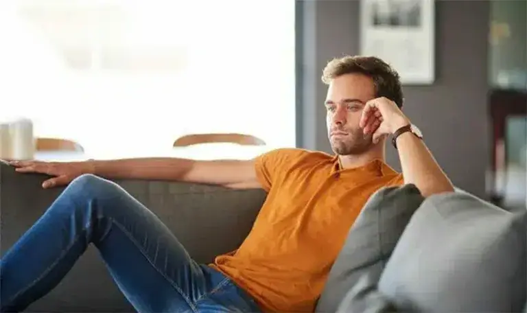 замислен млад човек седи на софа